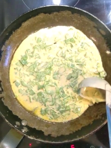Cooking the pancakes - a steel pan filled with a layer of spinach pancake batter poured in with a small metal ladle 